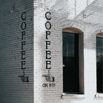 Coffee text signage with hand pointing painted onto a white brick wall 
